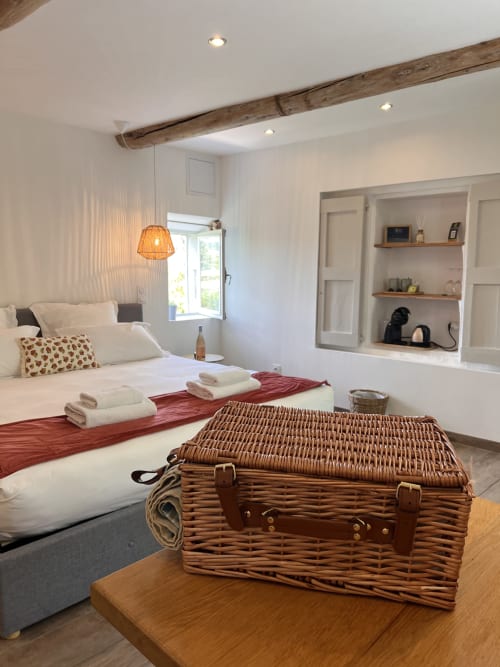 Chambre lumineuse à La Maison de Vaison avec poutres apparentes, vieille valise en osier, linges blancs et rangements intégrés