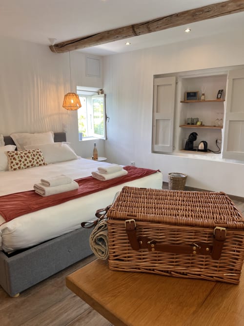 Chambre lumineuse à La Maison de Vaison B&B avec lit, poutre en bois, valise en rotin et rangements intégrés
