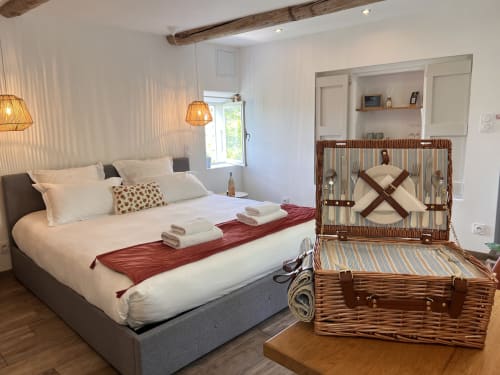 Chambre lumineuse à La Maison de Vaison avec lit confortable, malle en osier et poutres en bois rustique
