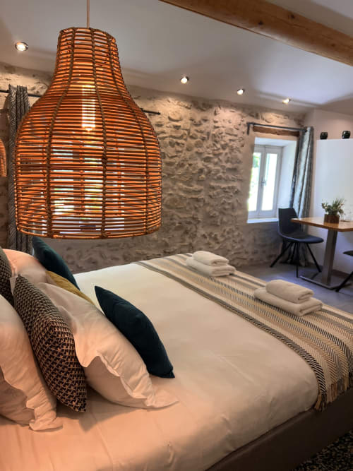 Chambre moderne à La Maison de Vaison avec suspension tressée, mur en pierre et literie blanche à Vaison-la-Romaine