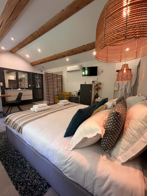Chambre moderne à La Maison de Vaison avec lit king-size, poutres apparentes, suspension en cuivre, salle de bain attenante et TV