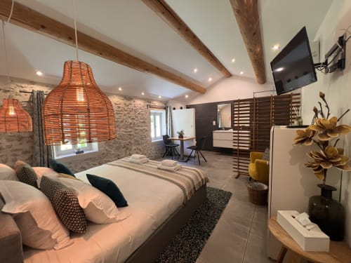 Chambre moderne à La Maison de Vaison avec lit queen, luminaire suspendu tissé orange, poutres apparentes, TV et style contemporain