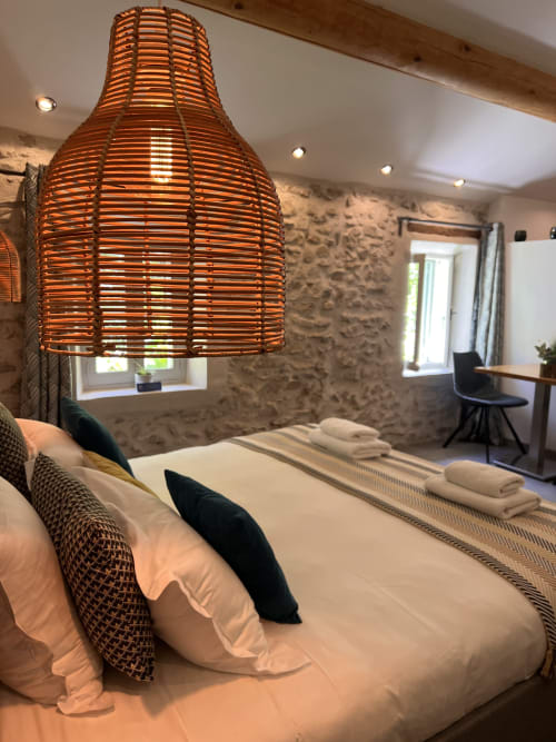 Chambre luxueuse à La Maison de Vaison B&B à Vaison-la-Romaine avec luminaire en rotin, murs en pierre texturée et
