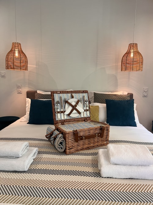 Chambre élégante à La Maison de Vaison avec luminaires en rotin, oreillers bleu marine et décoration de valises tressées