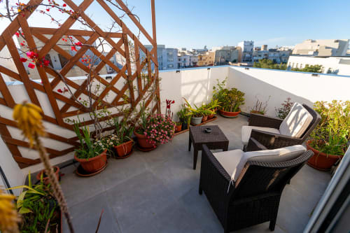 Rooftop terrace at Estrella Lodging in Rabat with black rattan seating, potted flowers, wooden trellis, and city skyline
