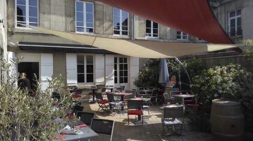 La Musardine En Vexin's shaded terrace with red and tan awnings, dining tables, and herb plants in Omerville