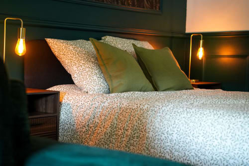 Chambre de luxe aux Séjours Ardennais avec lit queen-size, linge de lit motifs, coussins verts et luminaires suspendus