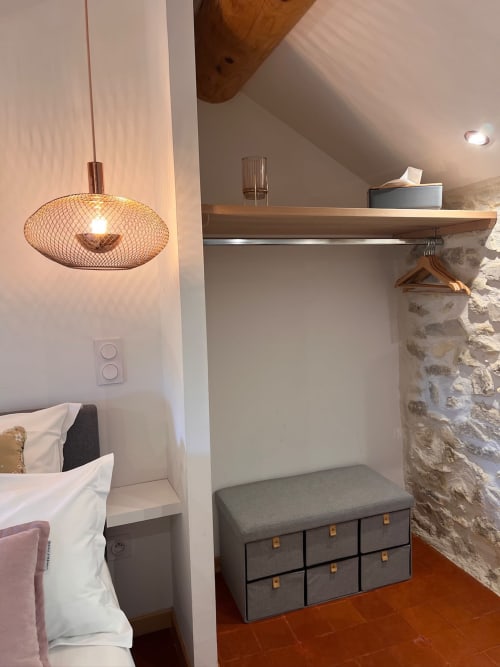 Chambre moderne à La Maison de Vaison B&B avec suspension luminaire, étagères bois et banc de rangement sur mur de pierre