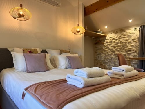 Chambre luxueuse à La Maison de Vaison avec literie blanche, serviettes roulées, luminaires suspendus et murs en pierre apparente