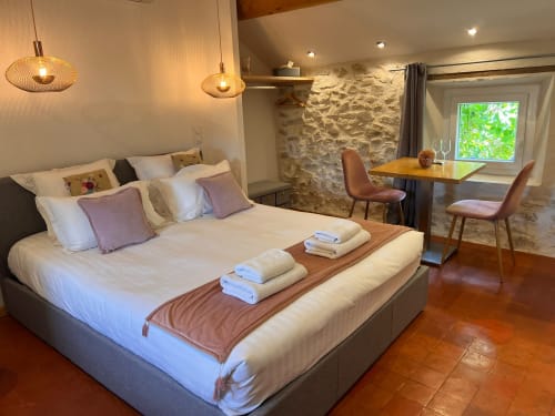 Chambre moderne à La Maison de Vaison avec lit queen-size, mur en pierre, bureau en bois, luminaires suspendus et vue sur le jardin