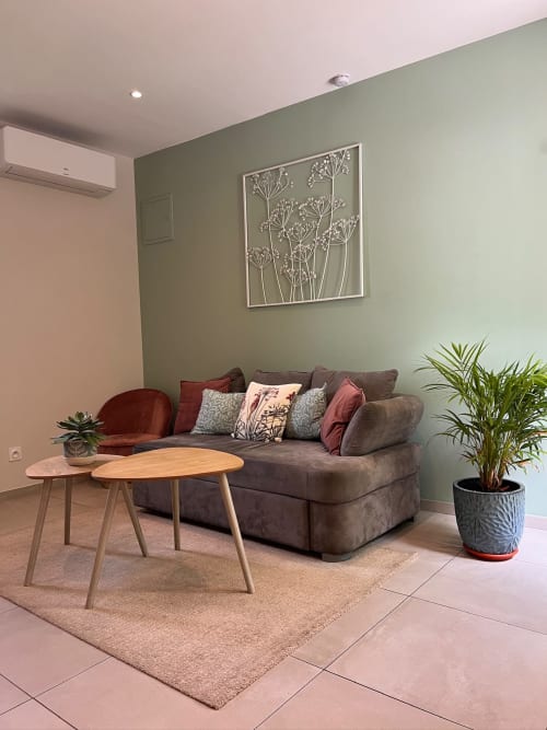 Salon moderne à La Maison de Vaison avec canapé gris, tables en bois, plantes en pot et art botanique mural