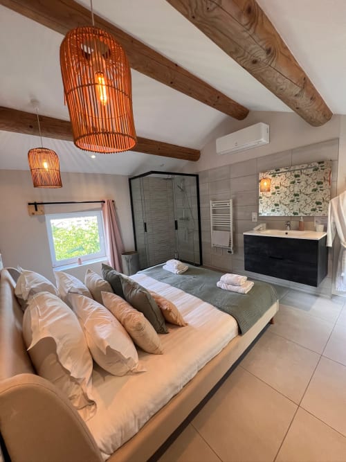 Chambre moderne de duplex à La Maison de Vaison avec lit, salle de bain attenante, poutres en bois et luminaires suspendus