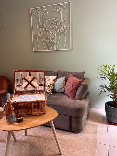 Salon douillet à La Maison de Vaison avec canapé gris capitonné, panier de pique-nique en osier, table en bois et art botanique mural