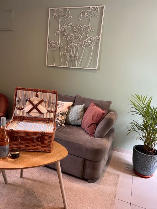 Salon accueillant à La Maison de Vaison avec canapé gris, panier de pique-nique en osier, art mural et plantes en pot