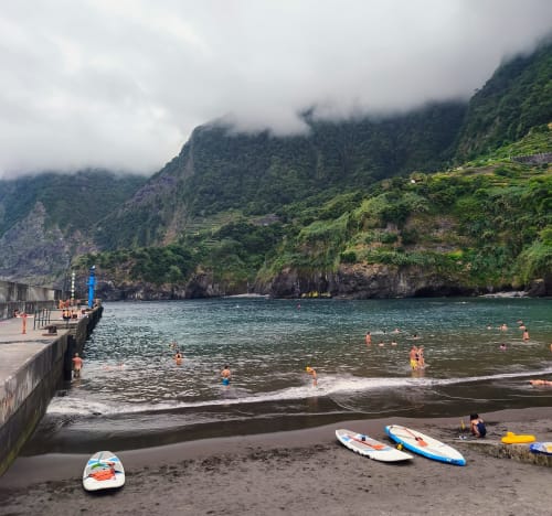 Praia de areia preta com falésias verdejantes, pranchas de paddle coloridas e banhistas em Les Terrasses Les Suites, Calheta
