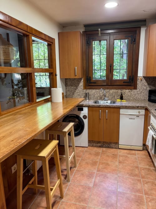 Cocina moderna con gabinetes de madera, encimera de granito, electrodomésticos de acero inoxidable y vistas al jardín en El Aserradero