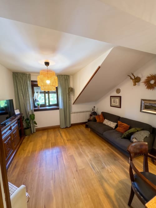 Acogedor salón de apartamento bajo techo en El Aserradero con suelos de madera, sofá oscuro, lámpara colgante y vistas al jardín en La Alberca
