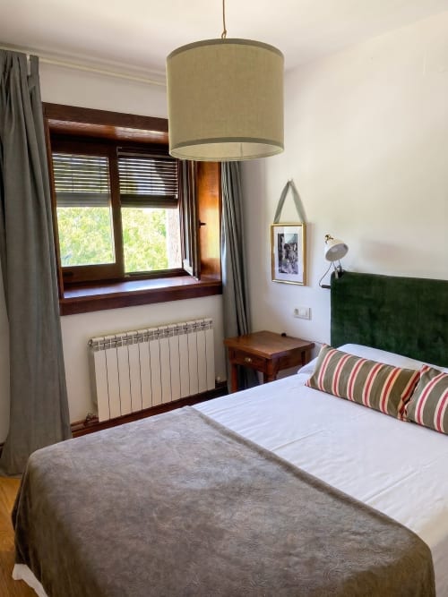 Dormitorio del apartamento Encina en El Aserradero, La Alberca, con cama, cabecero verde, lámpara colgante y vistas al jardín