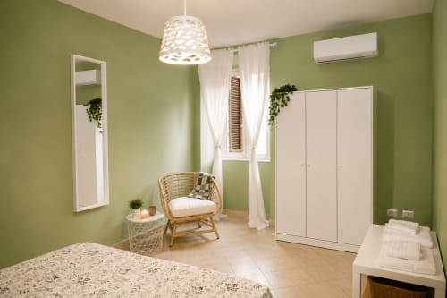 Camera da letto verde brillante negli Aparthotel Castelli a Castel Gandolfo con armadio bianco, sedia in rattan e lampada a sospensione moderna