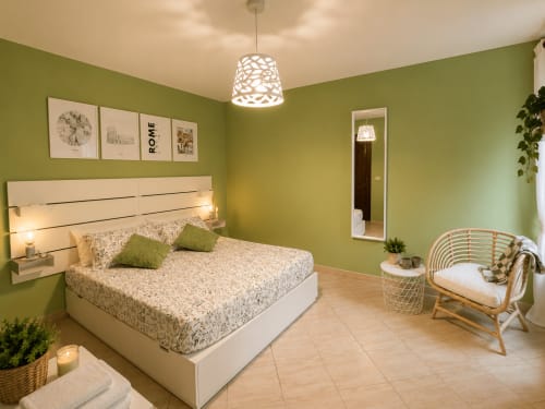 Camera luminosa verde salvia di Castelli Apartments a Castel Gandolfo con letto bianco moderno, sedia in vimini e lampade a sospensione