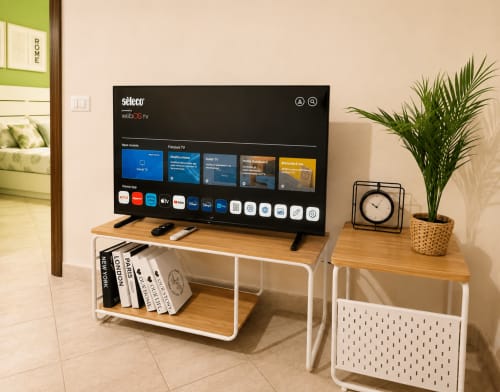 Soggiorno moderno con smart TV, mobile in legno, libri, pianta in vaso e orologio nell'appartamento Castrum Home a Castel