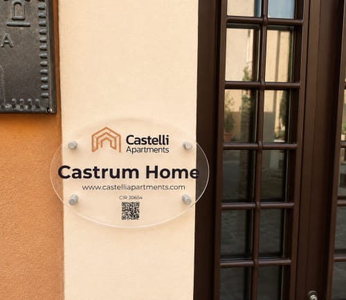 Insegna d'ingresso Castelli Apartments Castrum Home a Castel Gandolfo con codice QR e informazioni website su parete color crema