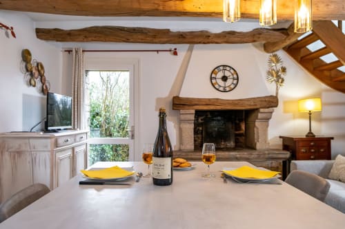 Salle à manger élégante à la Ferme de Kervihern avec poutres rustiques, cheminée et table dressée pour deux avec vin