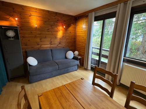 Séjour contemporain à Vars avec plafond à poutres apparentes, canapé bleu, table à manger et grandes fenêtres sur la forêt