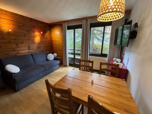 Appartement cosy à Vars avec table en bois, canapé bleu et vue sur les montagnes par les portes du balcon
