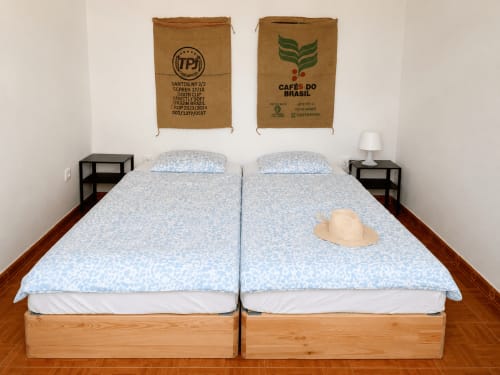 Duas camas gêmeas com roupa de cama azul estampada nas Villas Simone Porto Santo, decoradas com arte de parede feita de sacos de café brasileiros