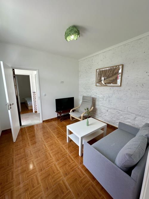 Sala de estar moderna dos apartamentos Villas Simone Porto Santo com sofá cinza, mesa de centro branca, piso de madeira e acabamentos branqueados