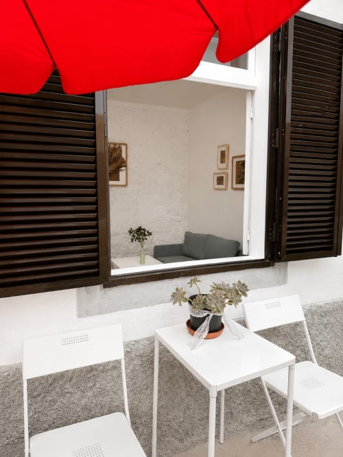Pátio do jardim privado da Casa da Anita com guarda-sol vermelho, cadeiras brancas e vista para o interior minimalista das Villas Simone