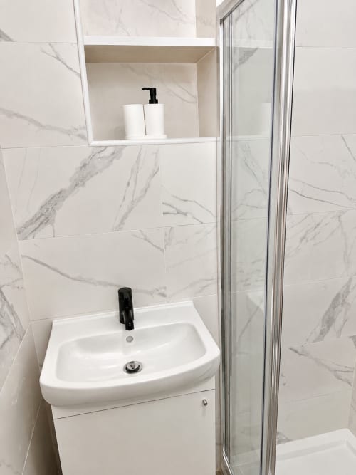 Pia de banheiro moderna com torneira preta, azulejos com efeito de mármore e prateleiras embutidas na Casa da Anita, Porto Santo