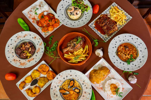 Gerechten van restaurant Balcón De Los Montés: gegrilde vis, tapas, patatas bravas, hummus en Spaanse specialiteiten op houten tafel