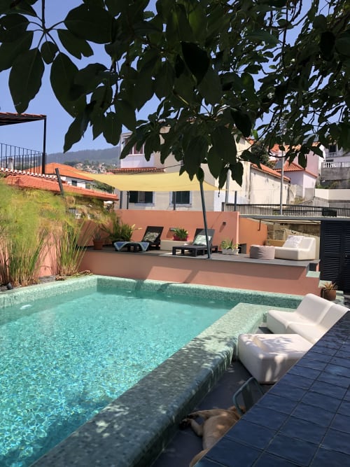 Piscina turquesa com espreguiçadeiras em Villas Simone, Funchal, cercada por edifícios em tons de terracota e vistas do oceano