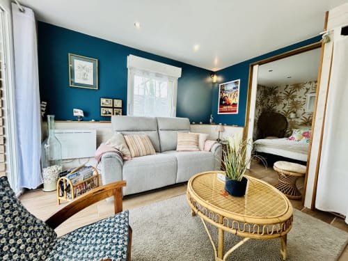 Das La Bounty Cottage in La Villa Plein Vent verfügt über ein graues Sofa, einen Rattantisch und eine türkisfarbene Akzentwand mit Gartenblick