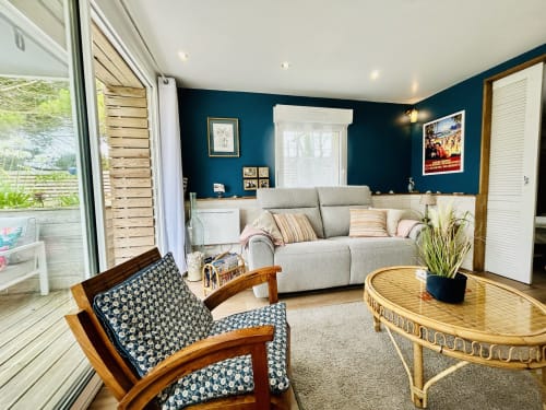 Wohnzimmer des La Bounty Cottage in La Villa Plein Vent, Barneville-Carteret, mit blauen Wänden, grauem Sofa und Holzstühlen