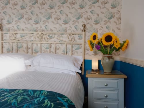 Deluxe king bed with white linens and ornate headboard at Douglas House B&B, featuring sunflowers on nightstand and