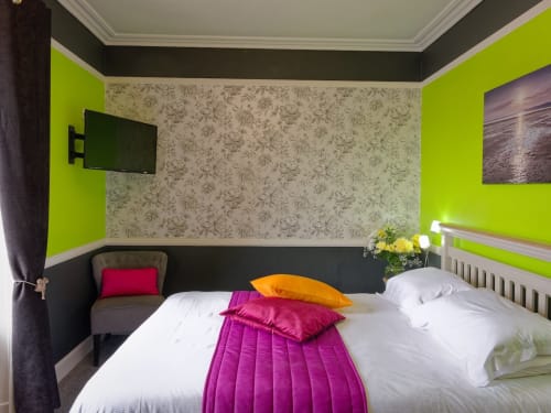 Bright modern bedroom at Douglas House B&B with lime green walls, floral wallpaper accent, king bed with colorful pillows,