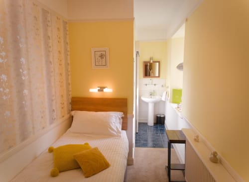 Bright yellow single bedroom at Douglas House B&B with white bedding, ensuite bathroom visible, and floral wallpaper in