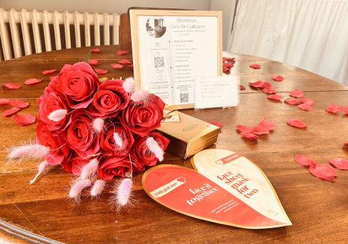 Installation romantique chez Chez Sir Guillaume avec roses rouges, pétales de rose et pancartes de bienvenue sur table en bois