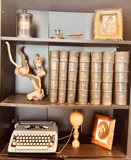 Bibliothèque vintage avec livres reliés cuir, machine à écrire, sculpture oiseau bois et objets décoratifs chez Romance