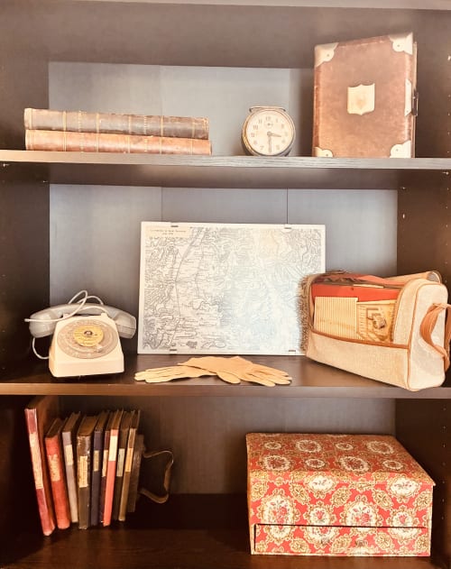 Étagères vintage présentant des livres anciens, téléphone rotatif, cartes, radio, valise et boîtes décoratives dans Romance chez