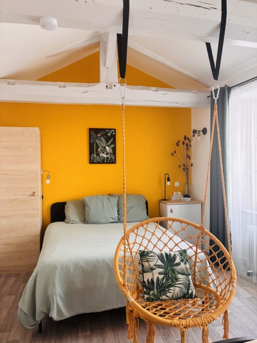 Chambre jaune éclatante aux Chez Mary Studios avec fauteuil suspendu en rotin, poutres blanches et mobilier moderne à Gannat