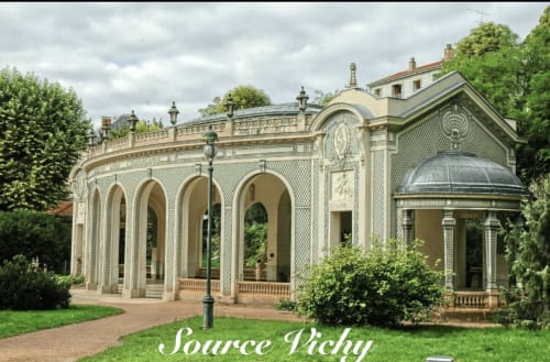 Élégant pavillon couleur crème aux colonnades cintrées entouré de verdure luxuriante en Provence, vue emblématique de Chez