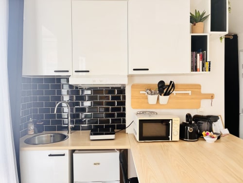 Kitchenette moderne du gîte Chez Mary Studios avec carrelage métro noir, armoires blanches, micro-ondes et bois