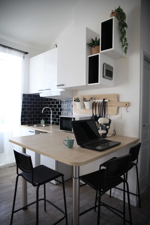 Cuisine-séjour moderne au gîte Chez Mary Studios en Provence avec table en bois, chaises noires et meubles blancs