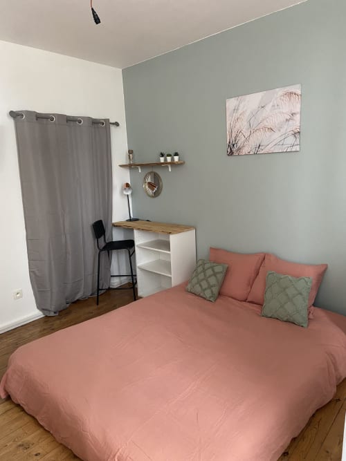 Chambre cosy aux Studios Chez Mary à Gannat avec lit corail, murs vert sauge, bureau en bois et œuvres d'art nature dans le sud de la France