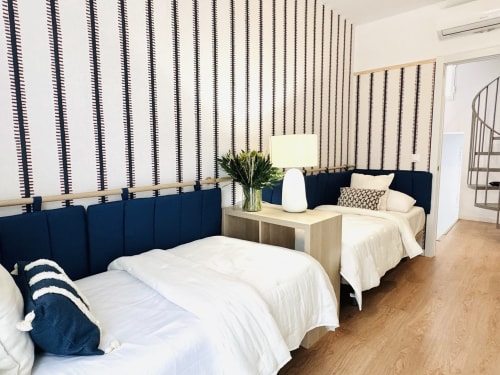 Dormitorio doble moderno en dúplex frente al mar en Málaga con cabeceros azul marino, ropa de cama blanca, pared de rayas y suelos de madera
