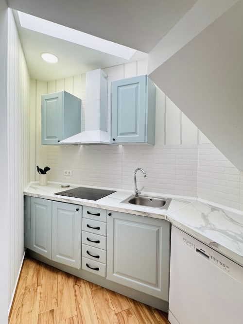 Cocina moderna en dúplex frente al mar en Málaga con muebles azul claro, azulejos blancos, encimera de mármol y madera